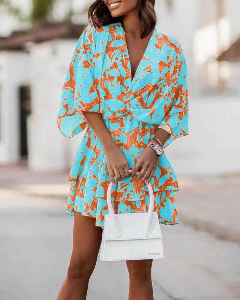 Frau in blau-orangefarbenem Blumenkleid mit weißer Handtasche, Sommermode, stilvoll, elegantes Outfit, Stadtbummel, modische Kleidung.