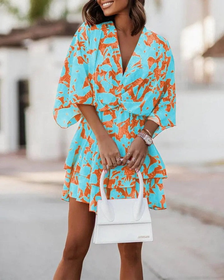 Frau in blau-orangefarbenem Blumenkleid mit weißer Handtasche, Sommermode, stilvoll, elegantes Outfit, Stadtbummel, modische Kleidung.