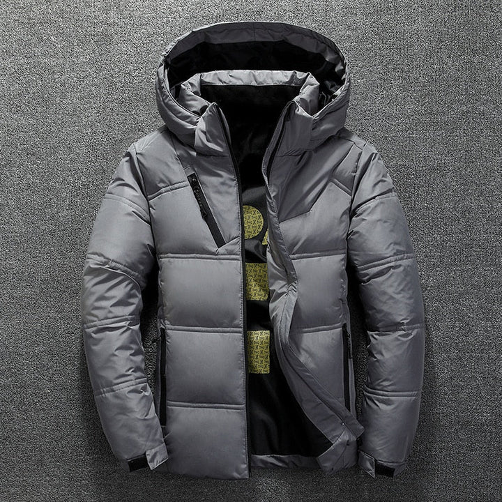 Graue Winterjacke mit Kapuze, Reißverschlusstaschen und gestepptem Design auf grauem Hintergrund. Herrenmode, warme Outdoor-Bekleidung.
