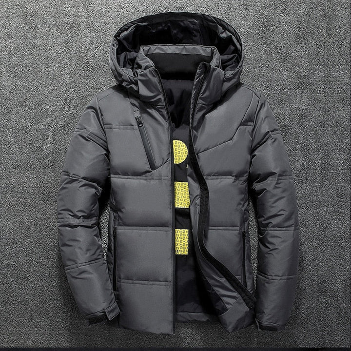 Graue Herren-Daunenjacke mit Kapuze, Reißverschluss und Steppmuster auf grauem Hintergrund. Wintermode, warme Outdoor-Bekleidung.