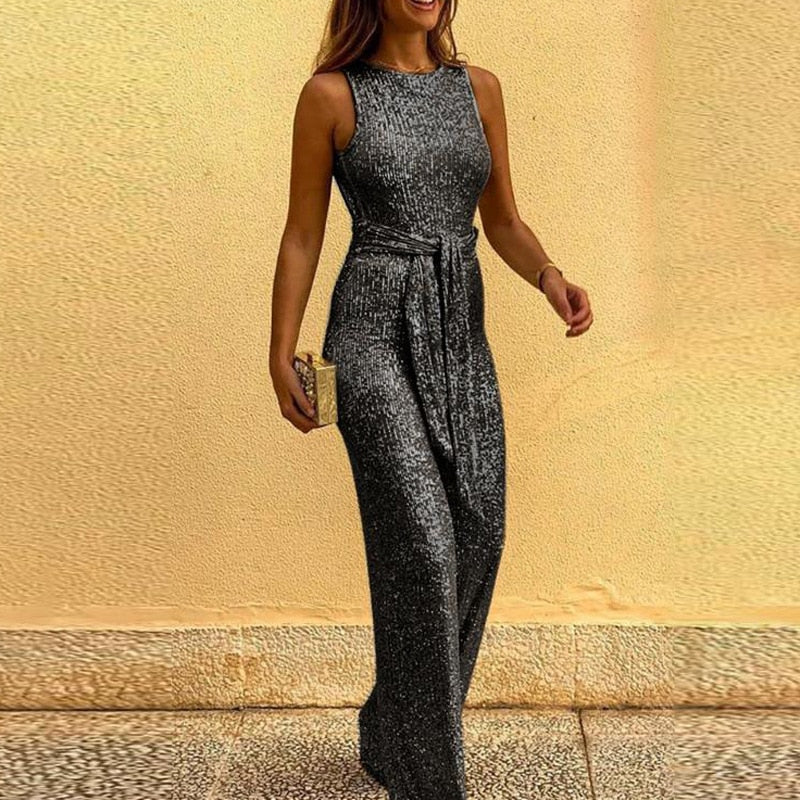Frau in elegantem, ärmellosem, bodenlangem, schwarzem Paillettenkleid mit Gürtel, hält eine goldene Clutch. Abendmode, glamouröser Look.