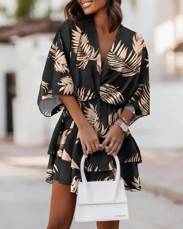 Frau in schwarzem Kleid mit beigem Palmenmuster, hält weiße Handtasche. Sommermode, elegantes Outfit, Freizeitkleidung, stilvoller Look.