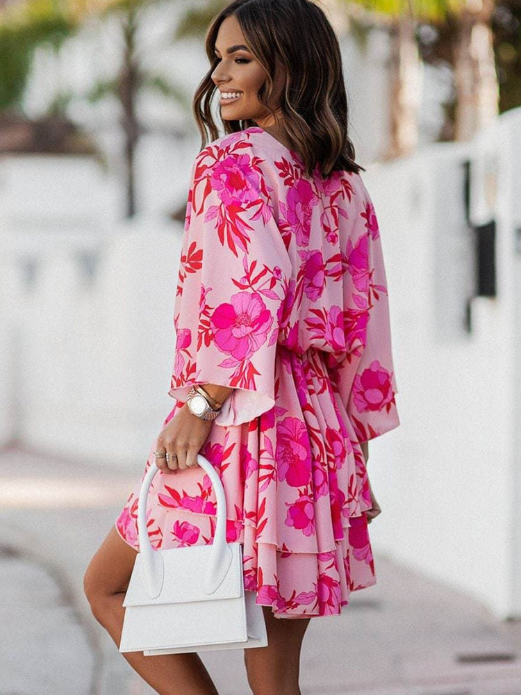 Frau in rosa Blumenkleid mit weißer Handtasche, lächelnd auf sonniger Straße. Modetrend, Sommerkleid, Damenmode, stilvoller Look.