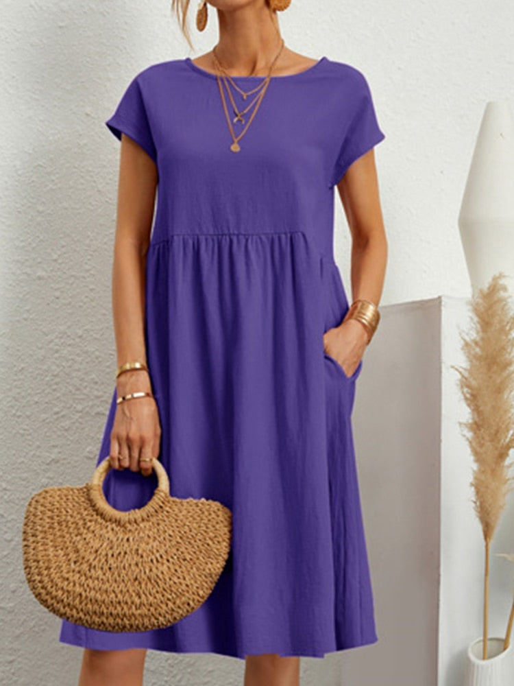 Frau in lila Sommerkleid mit kurzen Ärmeln, hält eine geflochtene Strohtasche. Goldene Accessoires, minimalistische Mode, eleganter Look.