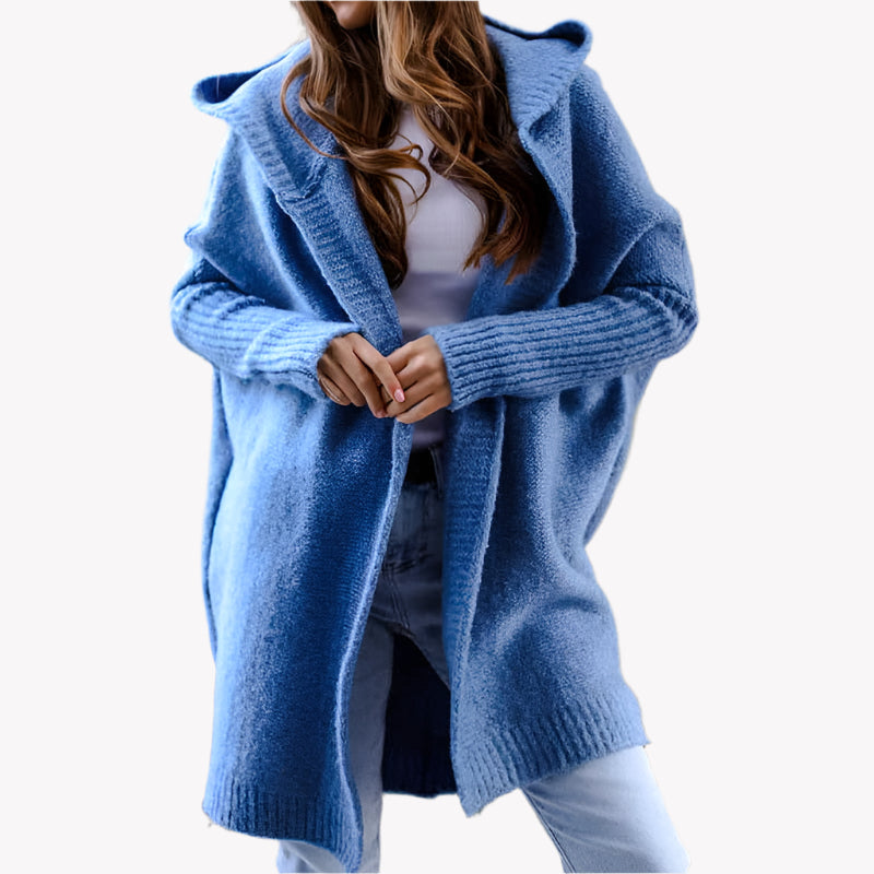 Frau in blauem Strick-Cardigan mit Kapuze, weißem Oberteil und Jeans vor einem weißen Hintergrund. Modischer Herbst-Look, gemütlicher Oversize-Stil.
