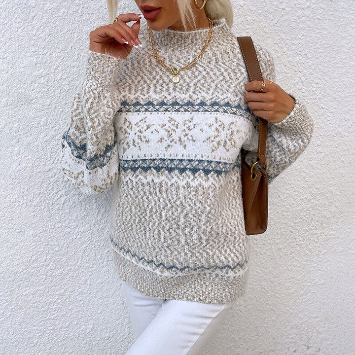 Frau in weißem Strickpullover mit blauem Muster, trägt goldene Halskette und Ohrringe, braune Tasche, vor weißer Wand. Wintermode, Strickmode.