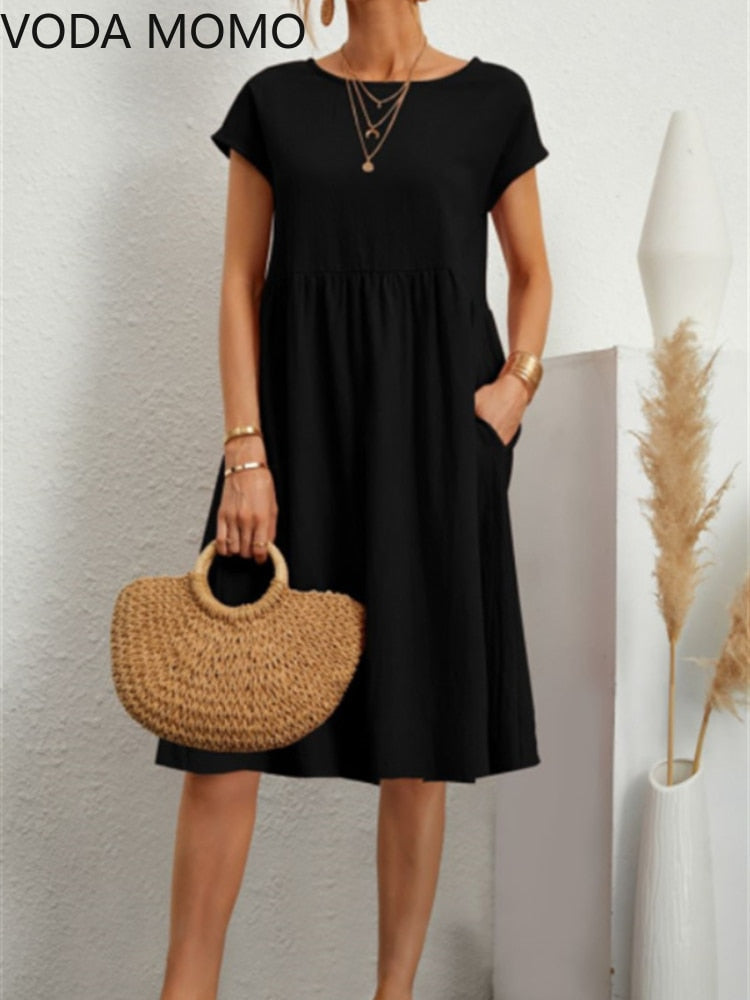 Frau in schwarzem Sommerkleid mit kurzen Ärmeln, hält runde Strohtasche. Minimalistischer Stil, Mode, Damenbekleidung, Accessoires.