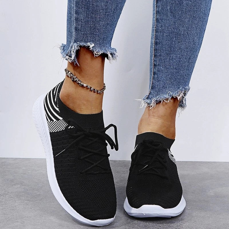 Schwarze Damen-Sneaker mit weißer Sohle, getragen mit zerrissenen Jeans. Modische Freizeitschuhe, ideal für Alltag und Sport.
