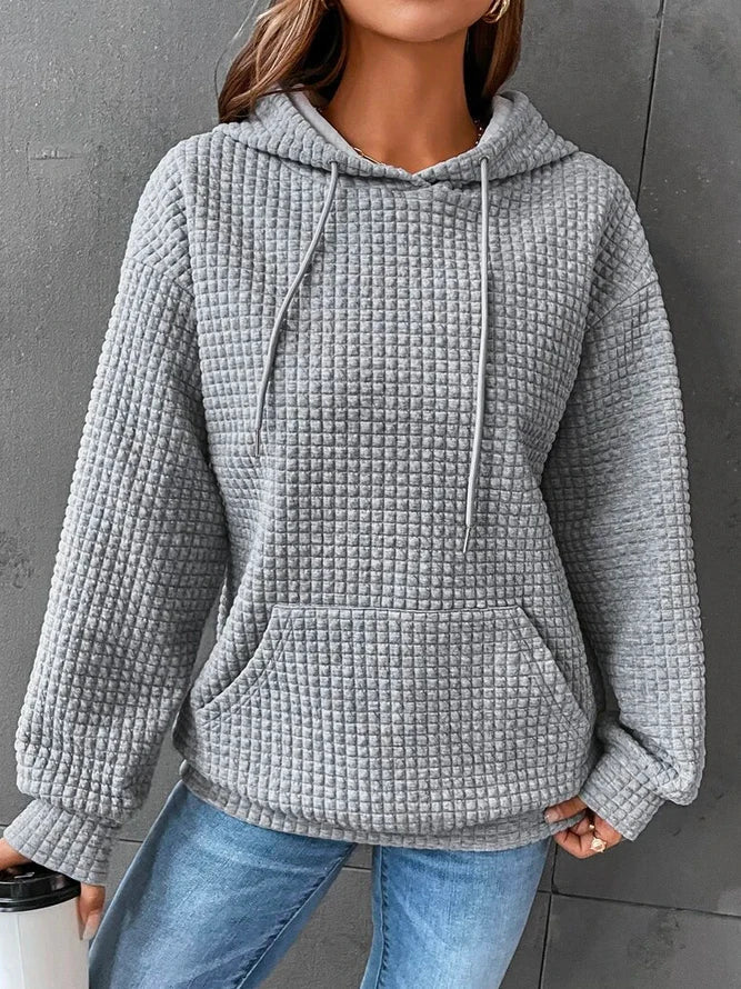 Grauer Kapuzenpullover mit Waffelstruktur, lässig geschnitten, kombiniert mit blauen Jeans. Perfekt für Herbstmode und gemütliche Outfits.
