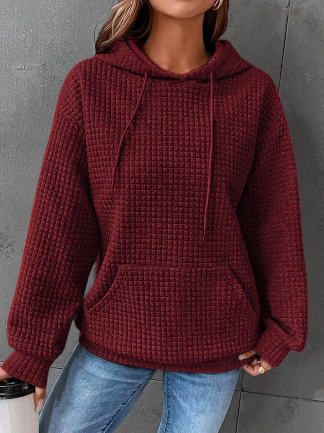 Frau in rotem Strickpullover mit Kapuze und Kängurutasche, trägt blaue Jeans, hält weißen Becher. Modetrend, Herbstmode, gemütlicher Look.