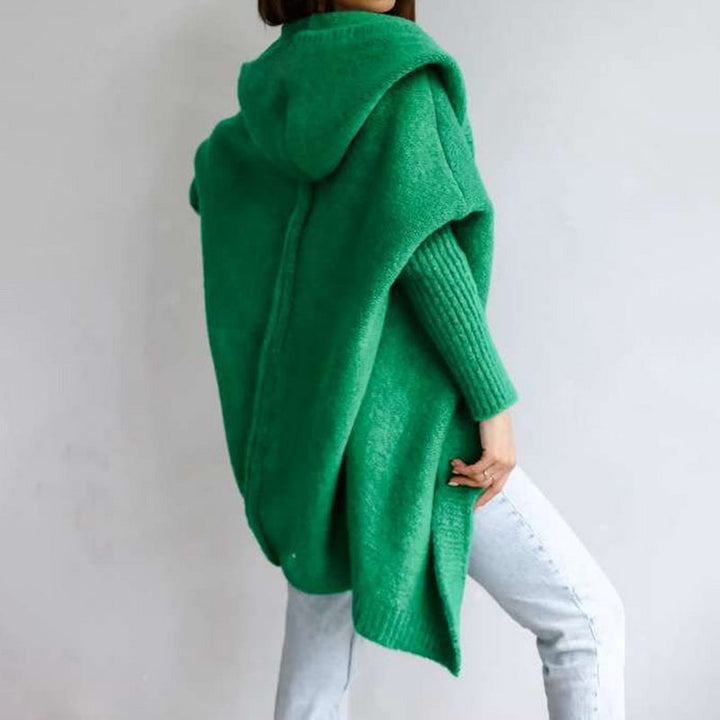 Grüner Strickponcho mit Kapuze, getragen von einer Person in blauer Jeans. Modischer, bequemer Poncho für Herbst und Winter.