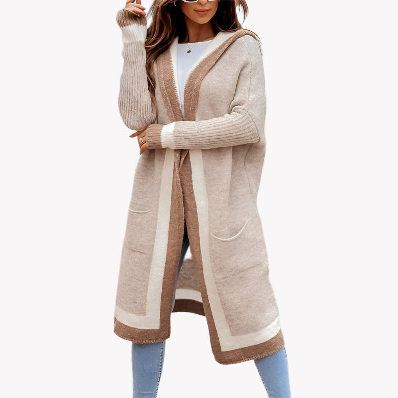 Frau in langer, beiger Strickjacke mit Kapuze und Taschen, mit blauen Jeans, vor einem weißen Hintergrund. Herbst 2025 Modetrend.