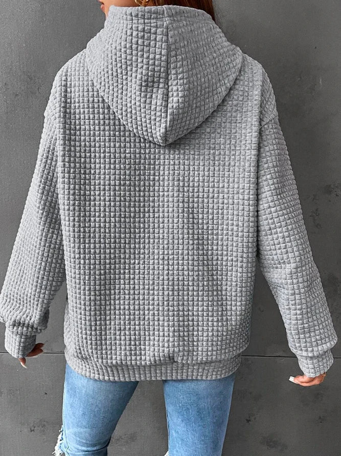 Frau in grauem, strukturiertem Kapuzenpullover aus Fleece, Rückansicht, lässiger Stil, kombiniert mit blauen Jeans, modische Freizeitkleidung.