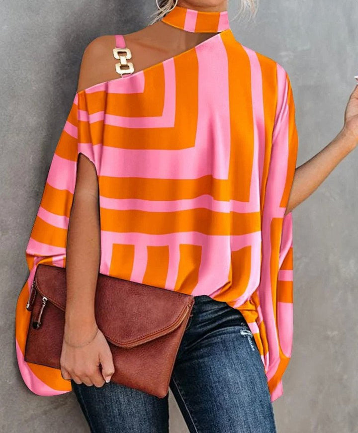 Frau in modischer, asymmetrischer Bluse mit orange-pinkem geometrischem Muster, hält braune Lederhandtasche, trägt Jeans. Trendige Damenmode.