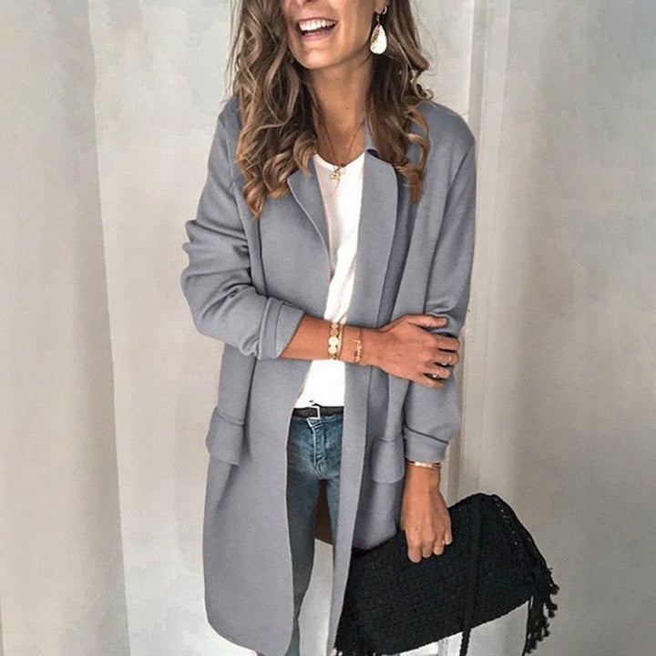 Frau in grauem Mantel, weißem Shirt und blauer Jeans, hält schwarze Tasche. Modetrend Herbst, stilvolle Damenbekleidung, lässiger Look.