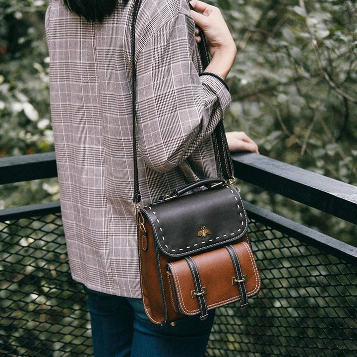Frau mit karierter Jacke trägt braune Ledertasche auf Balkon. Vintage-Mode, stilvolle Handtasche, Outdoor-Hintergrund.