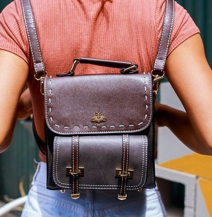 Frau mit stilvollem, braunem Lederrucksack mit Bienen-Emblem, modisch und praktisch für den Alltag. Perfekt für urbane Abenteuer und Reisen.
