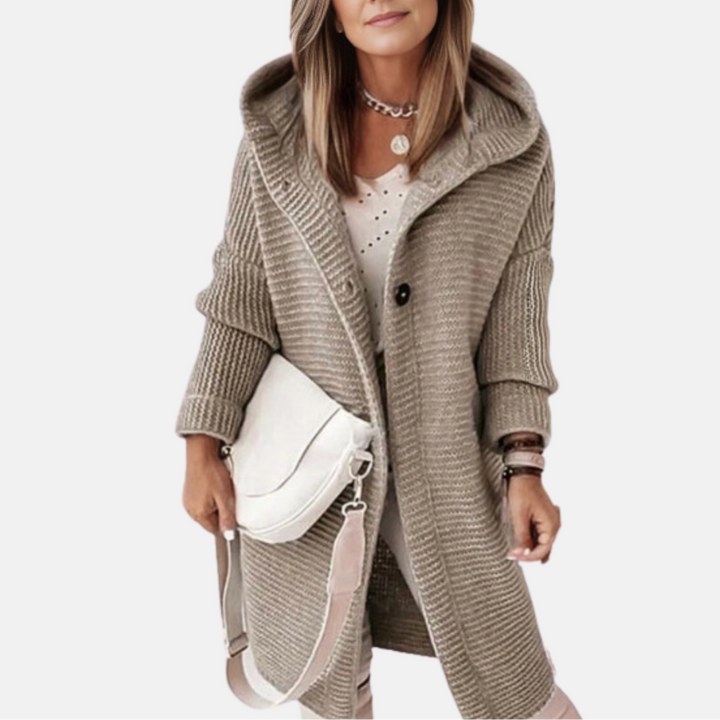 Eine Frau trägt einen beigen Strickmantel mit Kapuze und hält eine weiße Umhängetasche. Modetrend Herbst, Damenmode, Strickjacke.