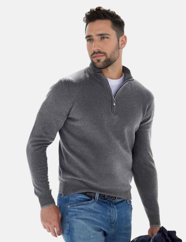 Mann in grauem Pullover mit Reißverschluss und blauer Jeans, hält Jacke. Mode für Herren, lässiger Look, Herbst-Winter-Kleidung.