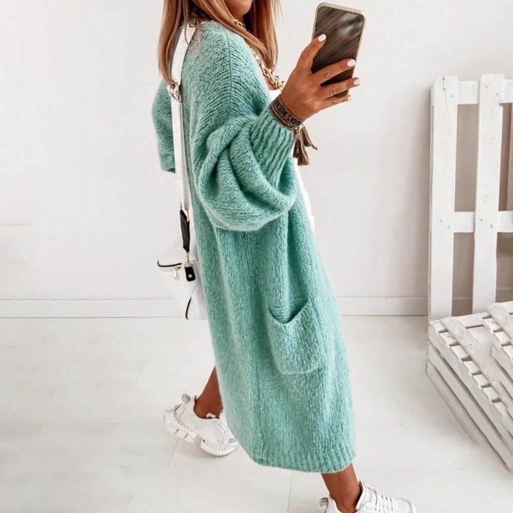 Frau in mintgrünem Strickcardigan macht Selfie, trägt weiße Sneakers und Umhängetasche. Modetrend, Herbstmode, lässiger Stil.