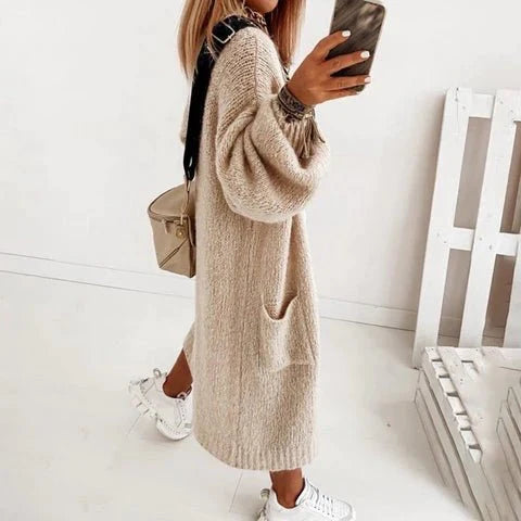 Frau in beigem Strickkleid mit langen Ärmeln, weißen Sneakers und brauner Umhängetasche macht Selfie. Modetrend Herbst, lässiger Stil.