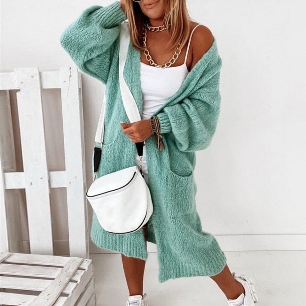 Frau in mintgrünem Strick-Cardigan, weißem Top und Sneakers, mit weißer Umhängetasche. Modetrend, lässiger Look, Herbstmode 2023.