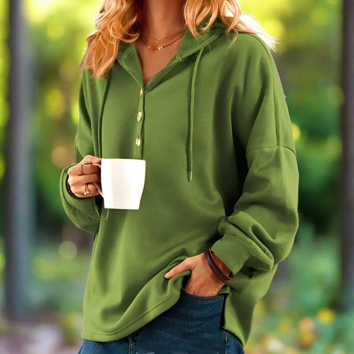 Frau in grünem Hoodie hält weiße Tasse, steht im Freien. Lässige Mode, Herbstkleidung, gemütlicher Stil. Entspannte Atmosphäre im Park.