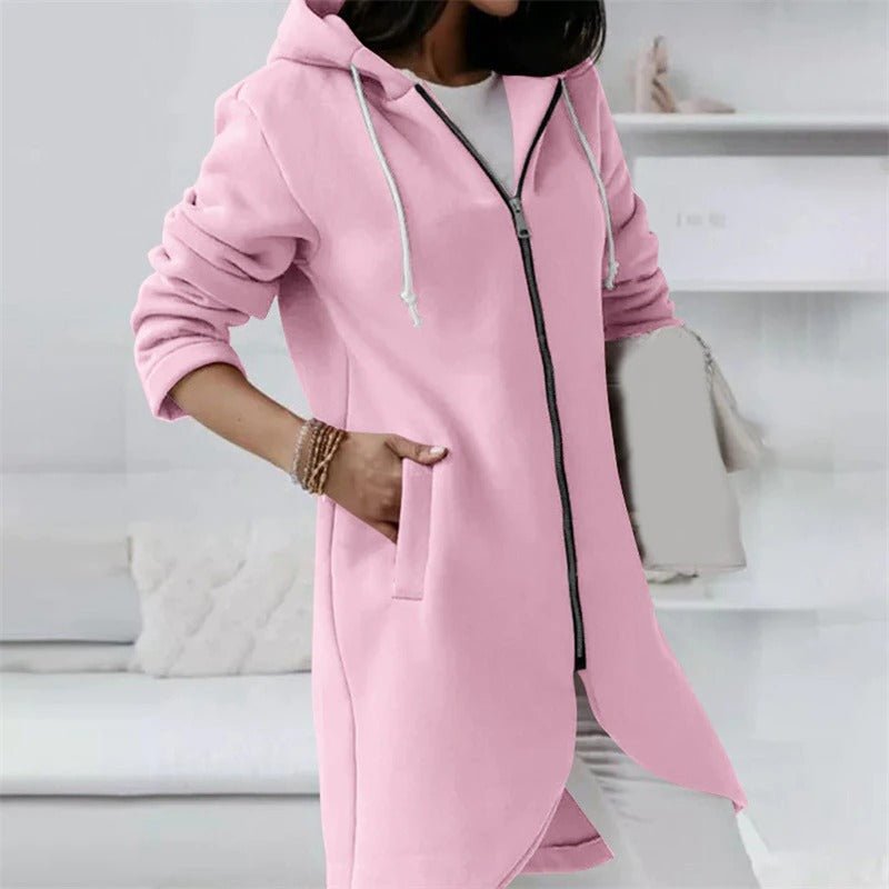 Frau in rosa Kapuzenjacke mit Reißverschluss und Taschen, lässiger Stil, modische Damenbekleidung, gemütliches Wohnzimmer im Hintergrund.