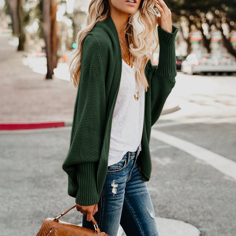 Frau in grüner Strickjacke und blauer Jeans auf Straße, hält braune Handtasche. Modetrend, lässiger Herbstlook, stilvolle Damenbekleidung.