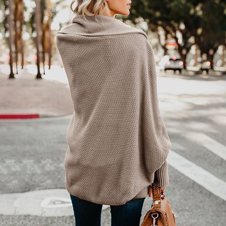 Frau in beigem Strickponcho auf Straße, Herbstmode, lässiger Stil, Rückansicht, modische Damenbekleidung, urbaner Hintergrund, Handtasche.