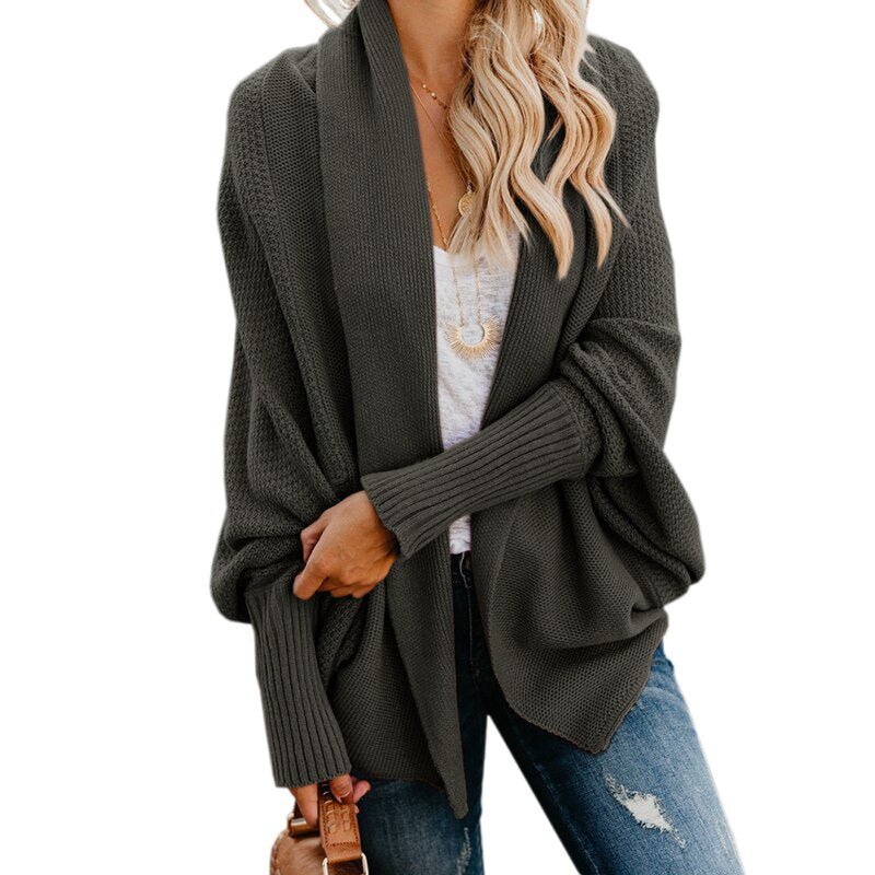 Frau in grauem Strick-Cardigan, weißem T-Shirt und blauen Jeans. Modischer Herbst-Look, lässiger Stil, lange blonde Haare.