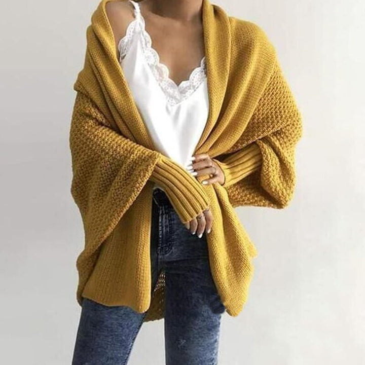 Frau trägt gelben Strick-Cardigan über weißem Spitzen-Top und blauer Jeans. Modischer Herbst-Look, gemütlicher Oversize-Stil.