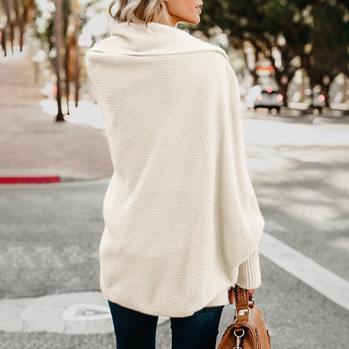 Frau in cremefarbenem Strickponcho auf Straße, hält braune Ledertasche. Herbstmode, stilvoller Look, Outdoor, urbane Umgebung.