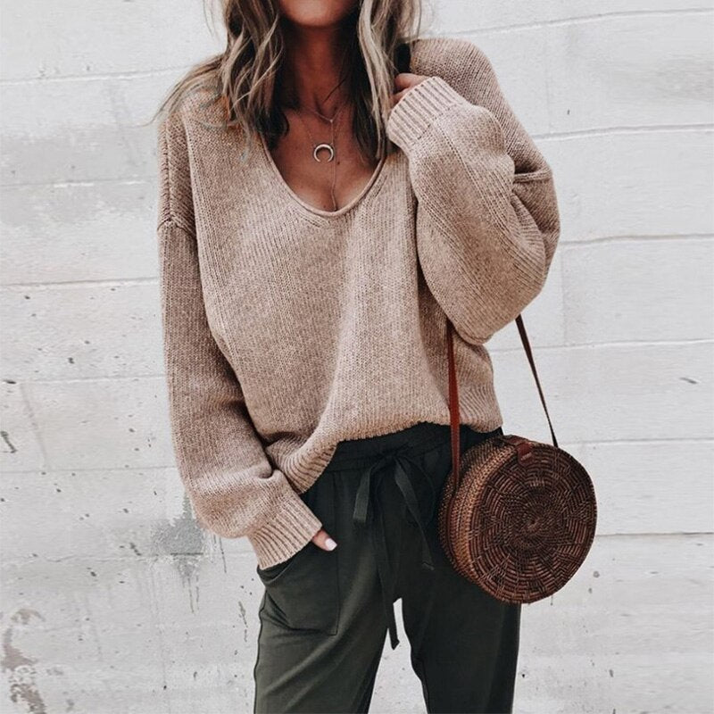 Frau in beigem Strickpullover mit V-Ausschnitt, trägt runde Strohtasche und olivgrüne Hose. Modetrend Herbst, lässiger Streetstyle-Look.