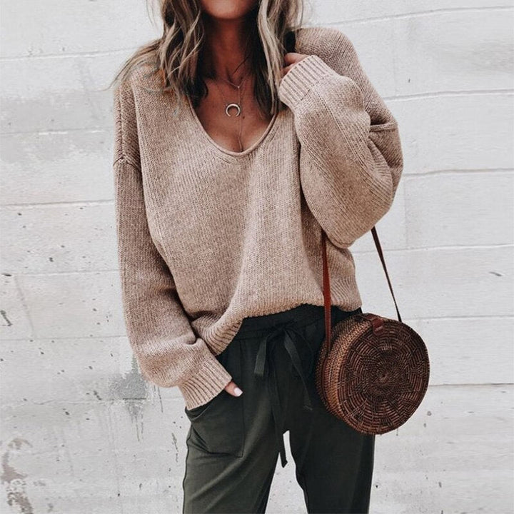 Frau in beigem Strickpullover mit V-Ausschnitt, trägt runde Strohtasche und olivgrüne Hose. Modetrend Herbst, lässiger Streetstyle-Look.