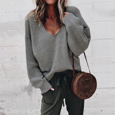 Frau in grauem Oversize-Pullover und olivgrüner Hose, trägt runde Strohtasche. Modetrend Herbst, lässiger Streetstyle-Look.