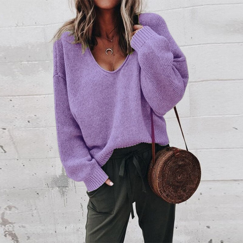 Frau in lila Pullover und olivgrüner Hose mit runder Strohtasche vor weißer Wand. Modetrend, lässiger Stil, Herbstmode.