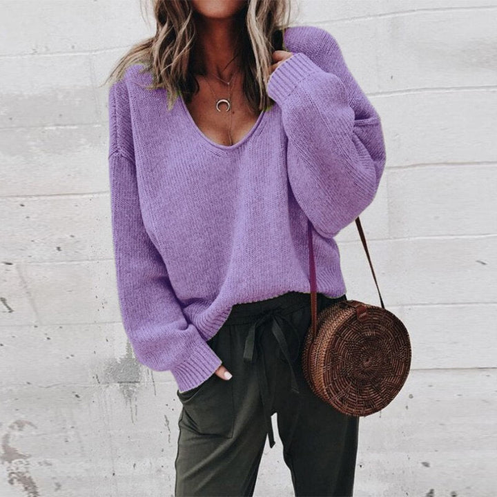 Frau in lila Pullover und olivgrüner Hose mit runder Strohtasche vor weißer Wand. Modetrend, lässiger Stil, Herbstmode.